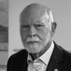 Greyscale photograph of J Craig Venter. Venter has a short white beard and is wearing a patterned suit jacket with a gold pin on one lapel over a light blue button-down shirt.