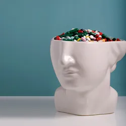 The lower half of a white ceramic head statue is filled with colorful pills to represent the placebo effect.