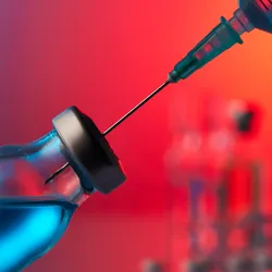 Image of a syringe inserted into a vial with a bluish liquid against a red background.