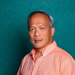 Ying K. Tam wears a pink collard shirt against a blue-green background.