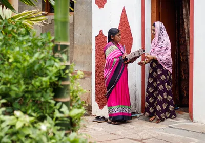 A community healthcare worker holds an informational booklet as she speaks about gestational diabetes with a young woman standing in a doorway.