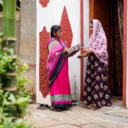 A community healthcare worker holds an informational booklet as she speaks about gestational diabetes with a young woman standing in a doorway.