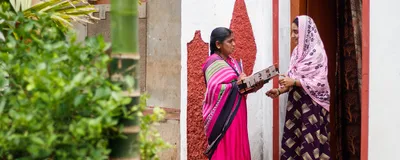 A community healthcare worker holds an informational booklet as she speaks about gestational diabetes with a young woman standing in a doorway.