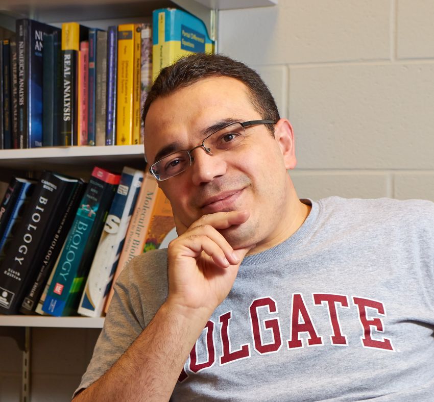 A photograph of Ahmet Ay in front of a bookshelf.