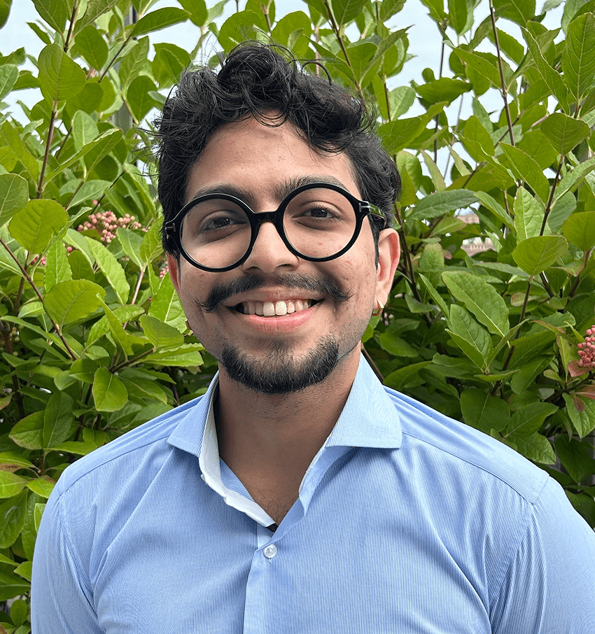 A photograph of Aziz Zafar wearing a blue shirt against a natural background.
