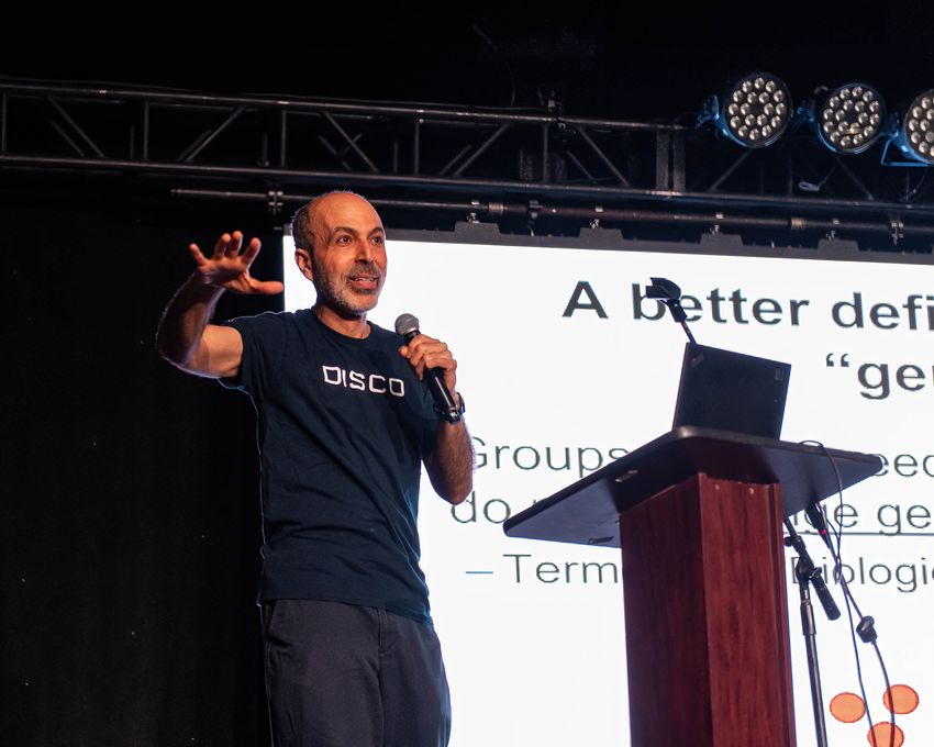 Mohamed Noor stands behind a lectern holding a microphone as he gives a talk on genetics at a scifi convention.