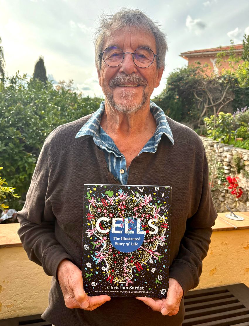Image of Chrisitan Sardet smiles for the camera as he holds his book.