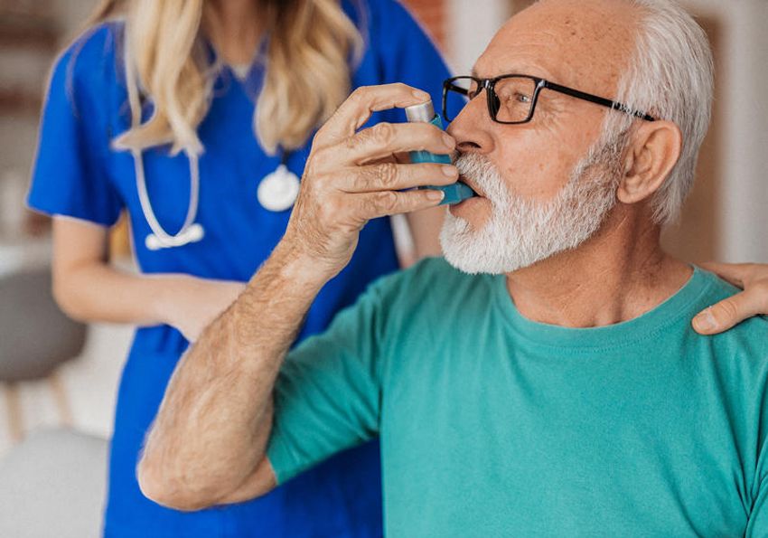 Photo of a man using an inhaler as a medical professional stands in the background