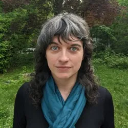 Carrie McDonough wears a blue scarf and a dark sweater in a headshot taken outside.