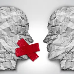 3D illustration of two human head shapes made on crumpled paper facing each other on a grey background. The head on the left has red tape covering its mouth, representing censorship. 