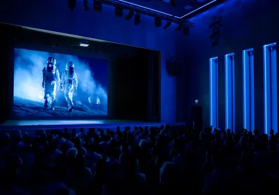 Photo of an unlit movie theater with a film showing two astronauts in space suits walking across a dusty surface. 