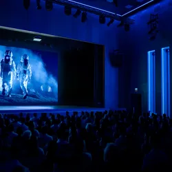 Photo of an unlit movie theater with a film showing two astronauts in space suits walking across a dusty surface. 