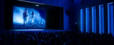 Photo of an unlit movie theater with a film showing two astronauts in space suits walking across a dusty surface. 