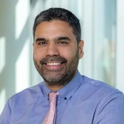 Andres Henao smiles while wearing a blue shirt and a pink tie in a headshot photo.