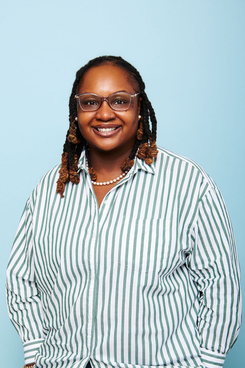 A photograph of Melanie McReynolds wearing a green striped shirt against a blue background. A photograph of Melanie McReynolds wearing a green striped shirt against a blue background.