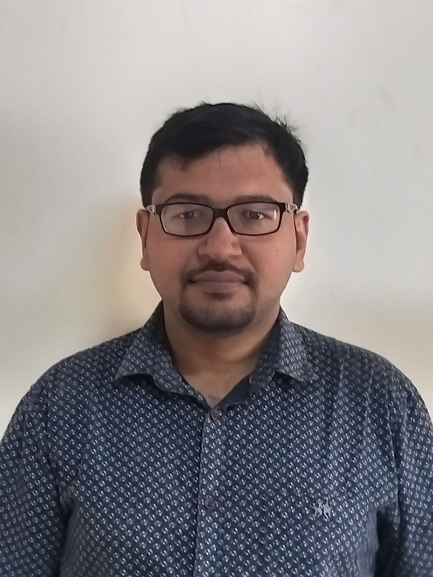 A photograph of Achal Agrawal wearing a printed shirt and glasses against a beige background. A photograph of Achal Agrawal wearing a printed shirt and glasses against a beige background.