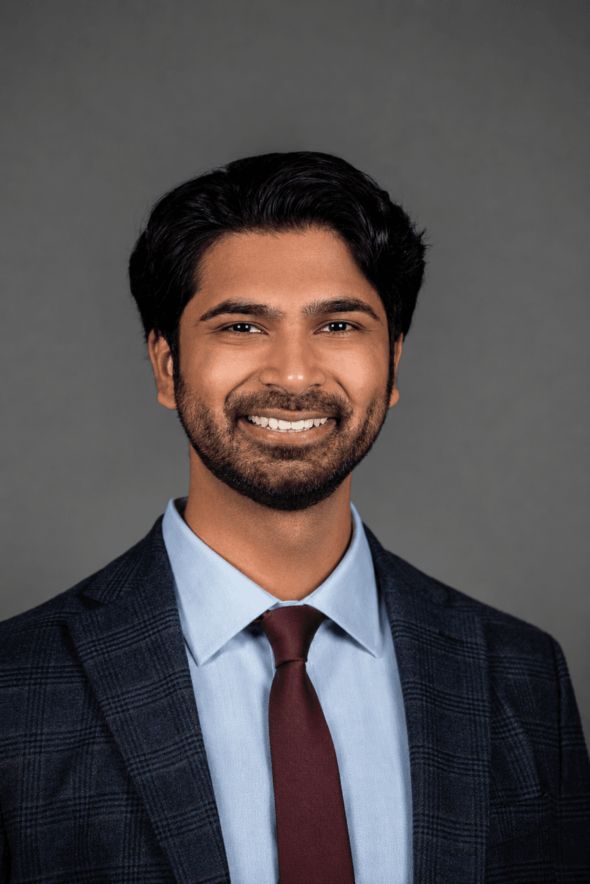 A photograph of Sankirth Madabhushi wearing a blazer, blue shirt, and maroon tie, against a grey background.