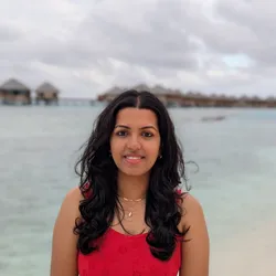 Kavi Bharathi R, PhD stands in a red top in front of the ocean.