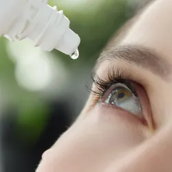 A woman puts an eye drop into her eye.