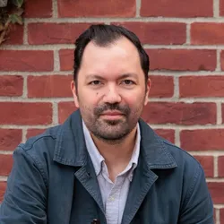 Patrick Boyle wears a dark jacket while standing in front of a brick wall.