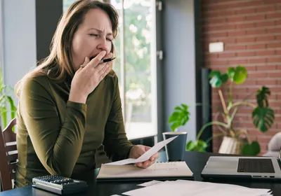Photo of a person in green top yawning at a desk, signifying sleep deprivation, which increases the density of synapses. 