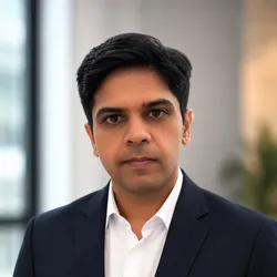 Kartik Sunagar wears a white collard shirt and a dark suit jacket in a headshot.