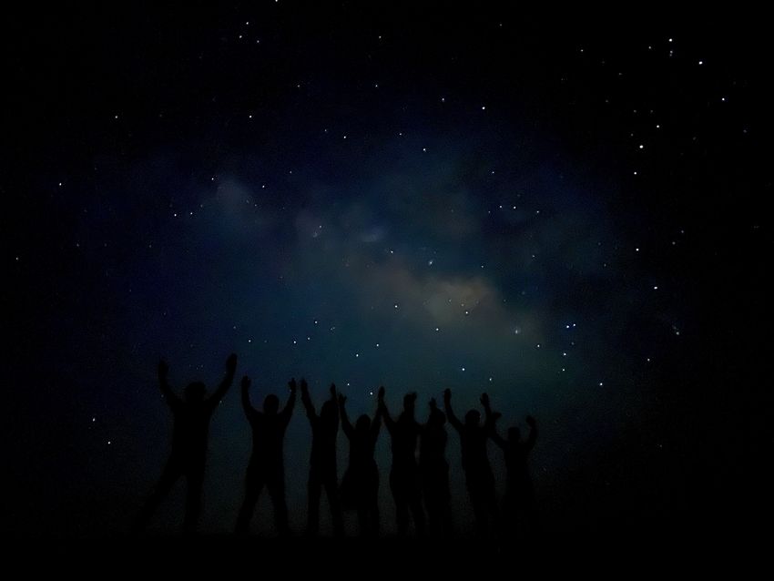 People stand in silhouette in front of the Milky Way visible in the night sky. People stand in silhouette in front of the Milky Way visible in the night sky.