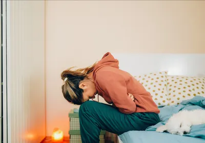 A woman doubles over in pain on her bedside, representing IBS pain.