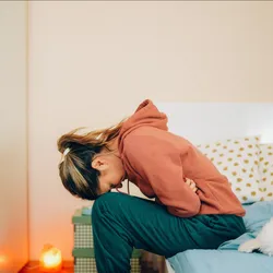 A woman doubles over in pain on her bedside, representing IBS pain.