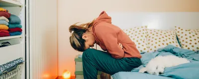 A woman doubles over in pain on her bedside, representing IBS pain.