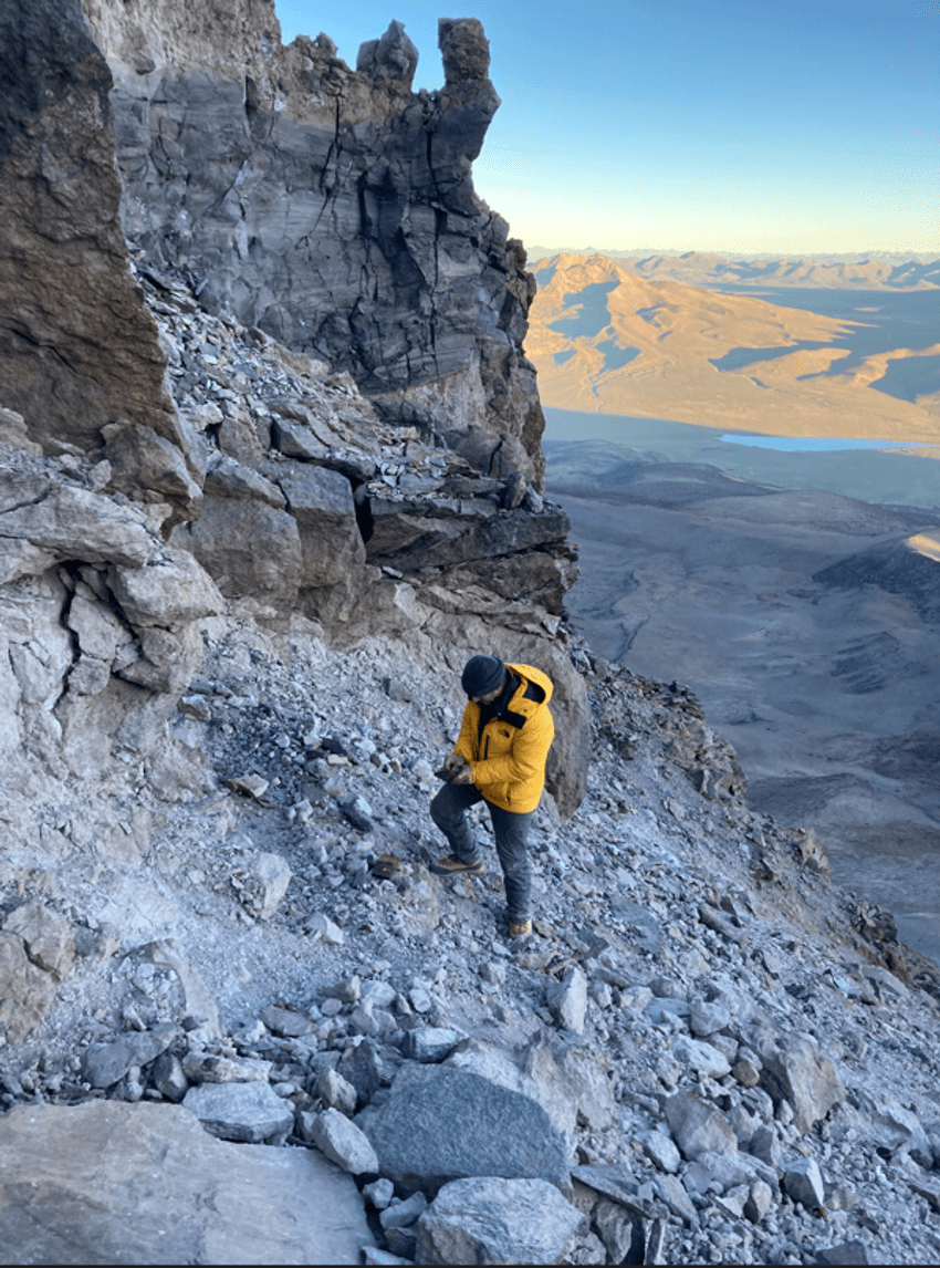 A researcher stands on the side of a rocky volcano setting mouse traps.