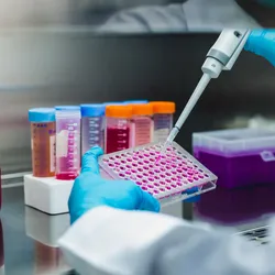 Researcher pipetting cell culture samples into a multiwell plate for in vitro drug screening