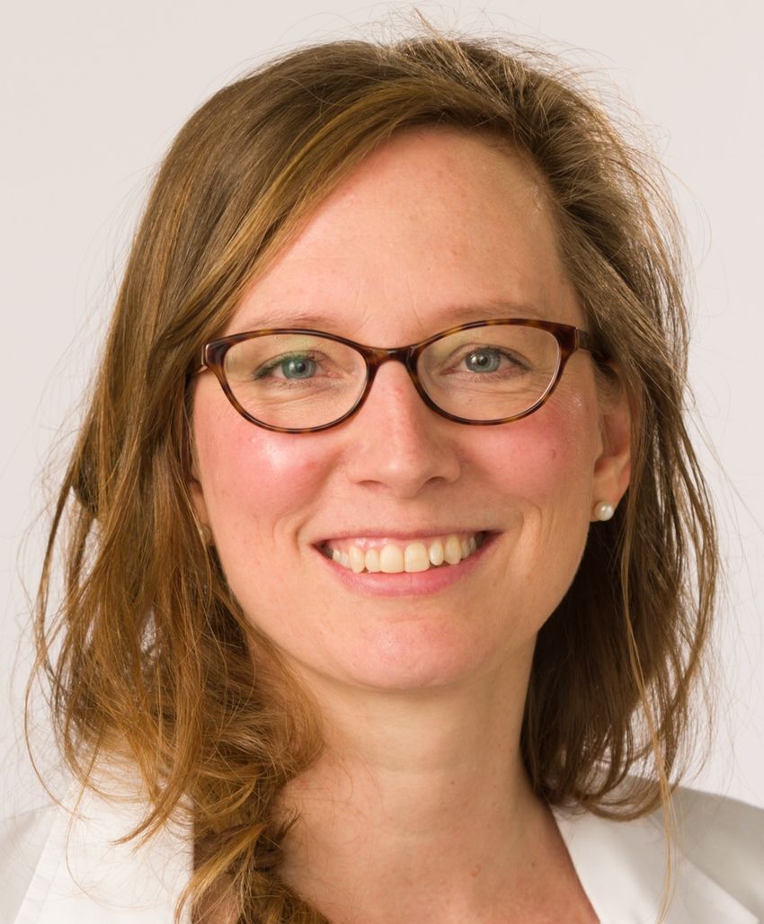 A woman wearing glasses smiles at the camera.