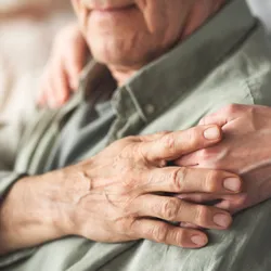 A carer supports the hand of an older man who is seated.