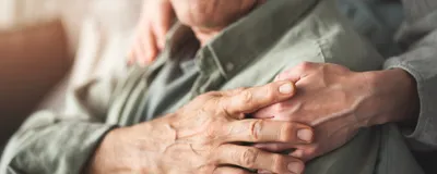 A carer supports the hand of an older man who is seated.