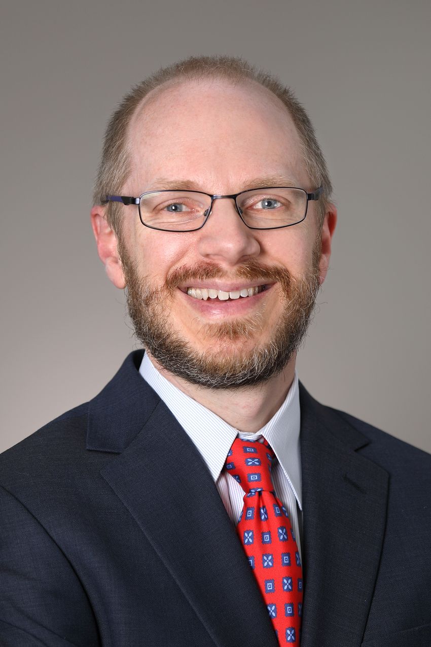 A man in a black suit and red tie smiles.