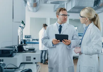 A photo of a male and female scientist discussing data on a tablet in a laboratory.