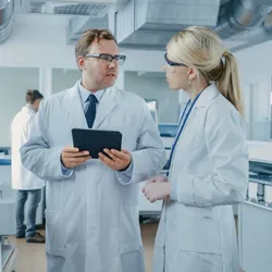 A photo of a male and female scientist discussing data on a tablet in a laboratory.