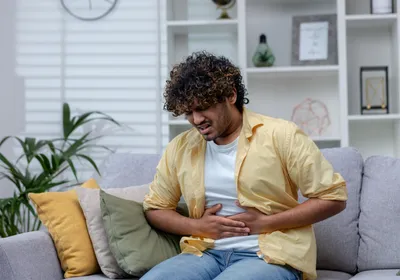 Man sick at home sitting on sofa, indicating he may be suffering from a Cyclospora infection. 