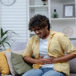 Man sick at home sitting on sofa, indicating he may be suffering from a Cyclospora infection. 