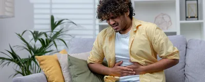 Man sick at home sitting on sofa, indicating he may be suffering from a Cyclospora infection. 
