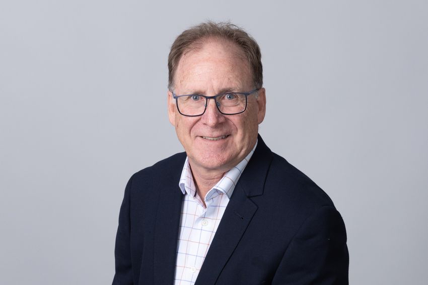 Malcolm Jones smiles wearing glasses, a black jacket, and a white shirt.