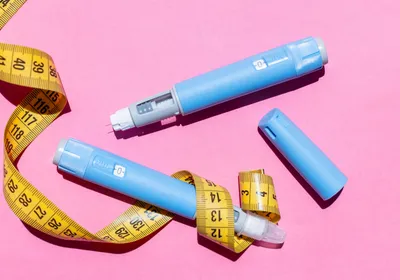 Blue Ozempic pens are shown with a yellow measuring tape on a pick background.