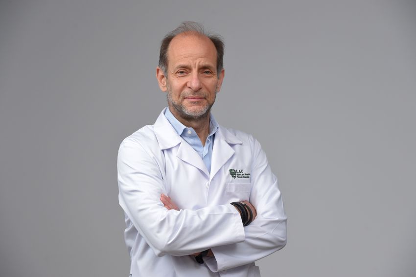 Andre Megarbane crosses his arms while wearing a white doctor’s coat in a portrait.