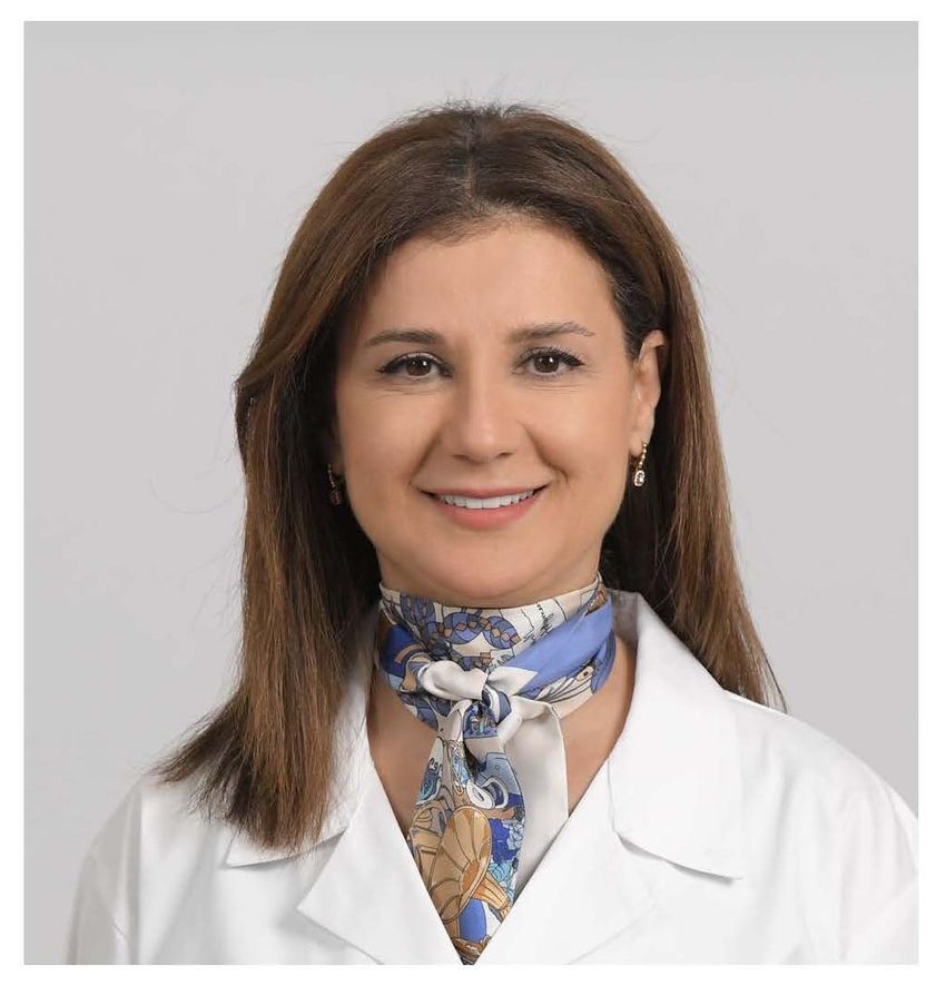 Sola Aoun Bahous smiles while wearing a white doctor’s coat in a headshot.