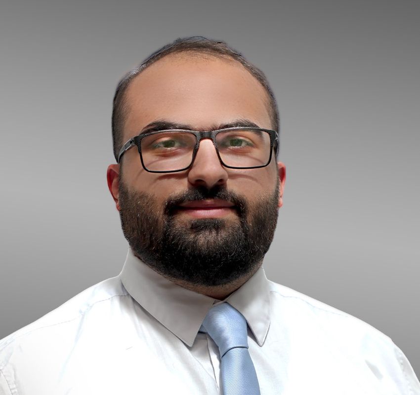 Ahmad Al-Bitar wears a white doctor’s coat and black glasses in a headshot.
