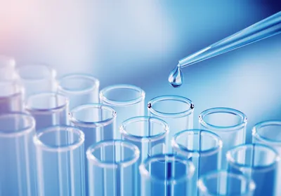 A droplet falling from a pipette tip above glass test tubes.