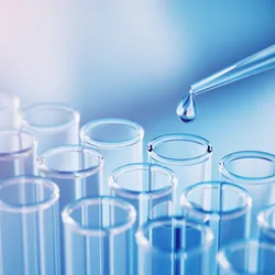 A droplet falling from a pipette tip above glass test tubes.