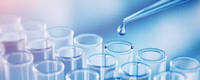 A droplet falling from a pipette tip above glass test tubes.