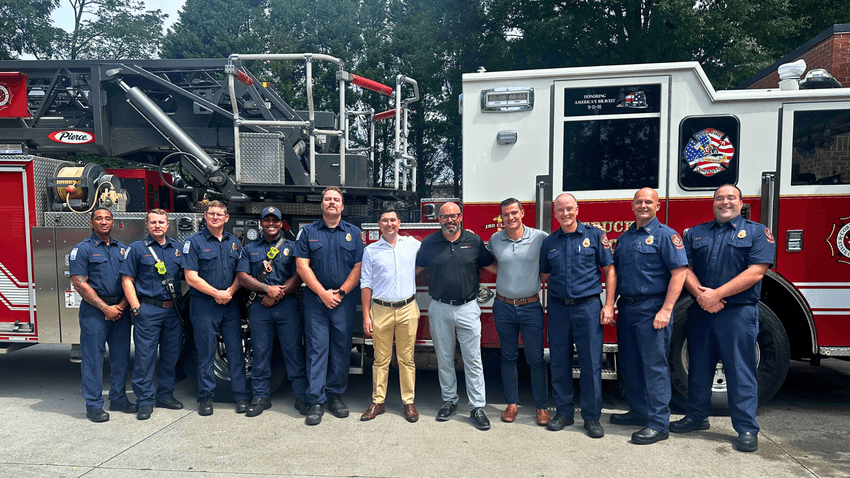 A photograph of Joe Landolina with first responders in front of a firetruck.